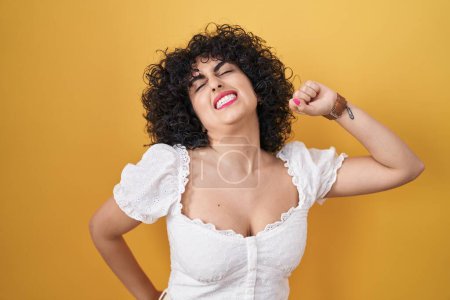 Photo for Young brunette woman with curly hair standing over yellow background stretching back, tired and relaxed, sleepy and yawning for early morning - Royalty Free Image