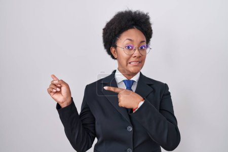Téléchargez les photos : Belle femme africaine avec des cheveux bouclés portant une veste d'affaires et des lunettes pointant de côté inquiet et nerveux avec les deux mains, expression concernée et surprise - en image libre de droit