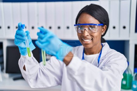 Foto de Joven mujer afroamericana científica sonriendo confiada sosteniendo tubos de ensayo en el laboratorio - Imagen libre de derechos