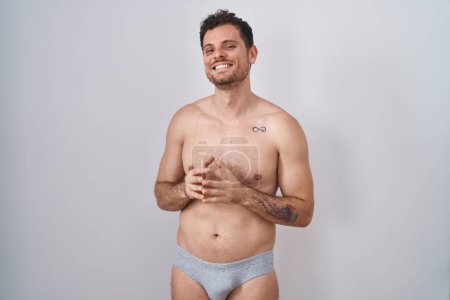 Photo for Young hispanic man standing shirtless wearing underware hands together and fingers crossed smiling relaxed and cheerful. success and optimistic - Royalty Free Image