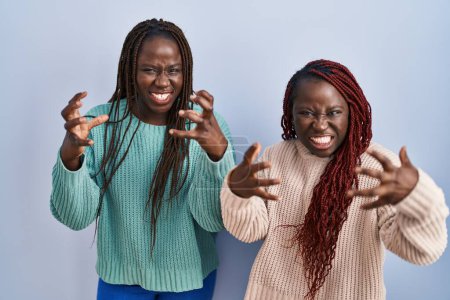 Photo for Two african woman standing over blue background shouting frustrated with rage, hands trying to strangle, yelling mad - Royalty Free Image