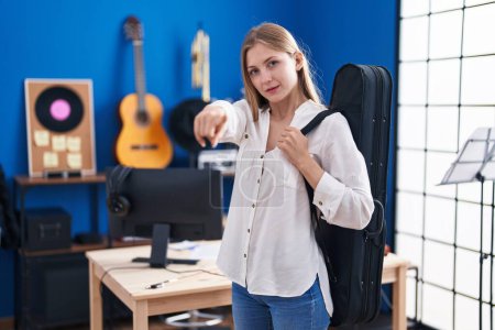Téléchargez les photos : Jeune femme caucasienne tenant étui de guitare pointant du doigt à la caméra et à vous, geste confiant regardant sérieux - en image libre de droit