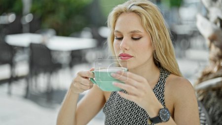 Téléchargez les photos : Jeune femme blonde tenant une tasse de café assis sur la table à la terrasse du café - en image libre de droit