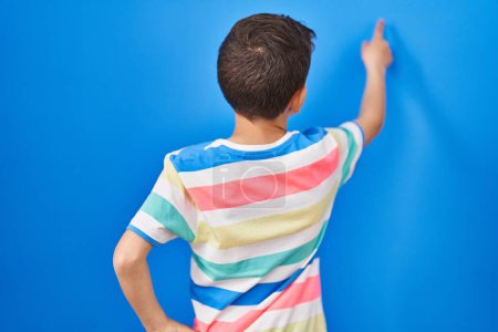 Photo for Young caucasian kid standing over blue background posing backwards pointing ahead with finger hand - Royalty Free Image