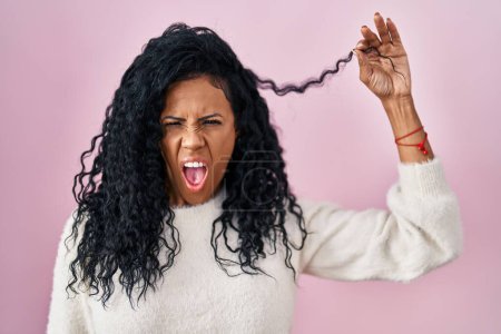 Téléchargez les photos : Femme hispanique du Moyen Âge tenant les cheveux bouclés en colère et fou hurlant frustré et furieux, criant de colère. rage et concept agressif. - en image libre de droit