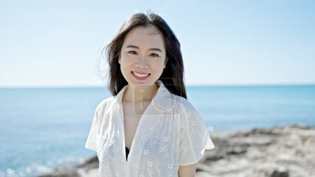 Foto de Joven mujer china sonriendo confiada de pie en la playa - Imagen libre de derechos