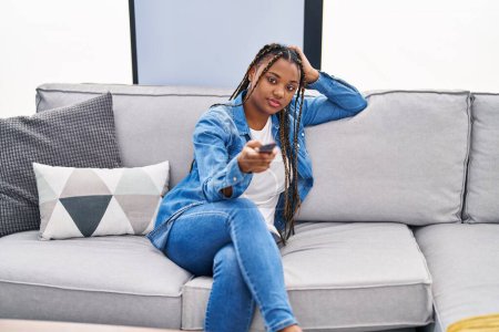 Foto de Mujer afroamericana viendo televisión sentada en un sofá con expresión aburrida en casa - Imagen libre de derechos