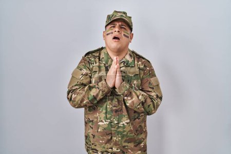Téléchargez les photos : Jeune homme hispanique portant uniforme de l'armée de camouflage mendier et prier avec les mains ainsi que l'expression de l'espoir sur le visage très émotionnel et inquiet. mendier. - en image libre de droit