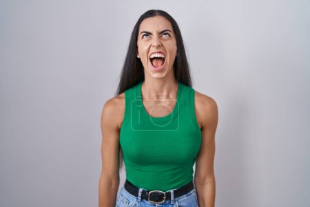 Foto de Young woman standing over isolated background angry and mad screaming frustrated and furious, shouting with anger. rage and aggressive concept. - Imagen libre de derechos