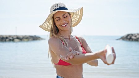 Foto de Joven turista rubia usando bikini aplicando crema solar en la playa - Imagen libre de derechos