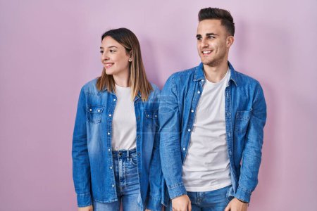 Téléchargez les photos : Jeune couple hispanique debout sur fond rose regardant de côté avec le sourire sur le visage, expression naturelle. riant confiant. - en image libre de droit