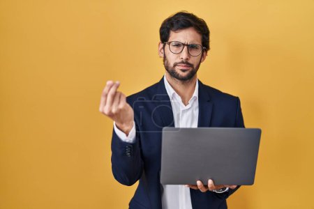 Foto de Hombre latino guapo trabajando con computadora portátil haciendo gesto italiano con la mano y los dedos expresión de confianza - Imagen libre de derechos