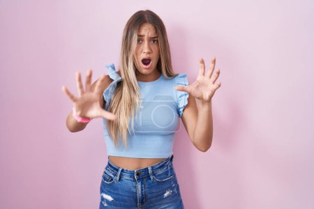 Téléchargez les photos : Jeune femme blonde debout sur fond rose effrayé et terrifié par l'expression de la peur arrêter geste avec les mains, criant sous le choc. concept de panique. - en image libre de droit