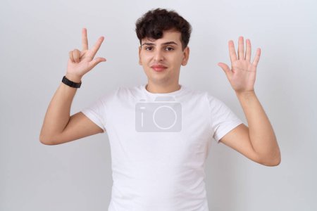 Junger Mann in lässigem weißem T-Shirt, der mit Finger Nummer acht zeigt und nach oben zeigt, während er selbstbewusst und glücklich lächelt. 