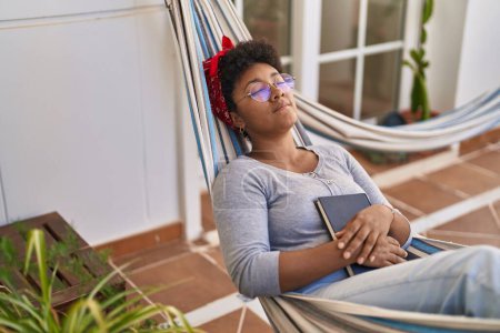 Photo for African american woman lying on hammock sleeping at home terrace - Royalty Free Image