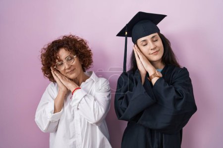 Photo for Hispanic mother and daughter wearing graduation cap and ceremony robe sleeping tired dreaming and posing with hands together while smiling with closed eyes. - Royalty Free Image