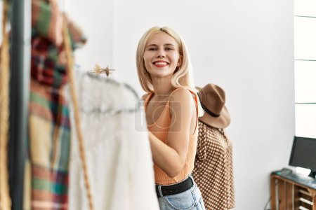 Photo for Young blonde woman customer choosing clothes smiling at clothing store - Royalty Free Image