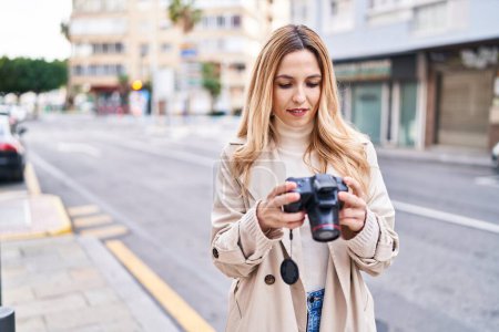 Téléchargez les photos : Jeune femme blonde souriant confiant en utilisant une caméra professionnelle à la rue - en image libre de droit