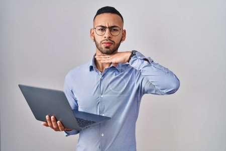 Téléchargez les photos : Jeune homme hispanique travaillant à l'aide d'un ordinateur portable couper la gorge avec la main comme couteau, menacer d'agression avec une violence furieuse - en image libre de droit