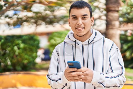 Téléchargez les photos : Jeune homme souriant confiant en utilisant smartphone au parc - en image libre de droit
