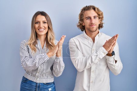 Téléchargez les photos : Jeune couple debout sur fond bleu applaudissant et applaudissant heureux et joyeux, souriant mains fiers ensemble - en image libre de droit