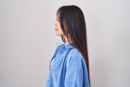 Téléchargez les photos : Jeune femme chinoise debout sur fond blanc regardant vers le côté, pose de profil relax avec visage naturel et sourire confiant. - en image libre de droit