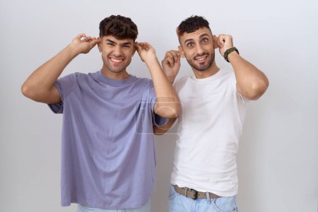 Photo for Homosexual gay couple standing over white background smiling pulling ears with fingers, funny gesture. audition problem - Royalty Free Image