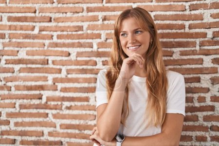 Photo for Young caucasian woman standing over bricks wall with hand on chin thinking about question, pensive expression. smiling and thoughtful face. doubt concept. - Royalty Free Image