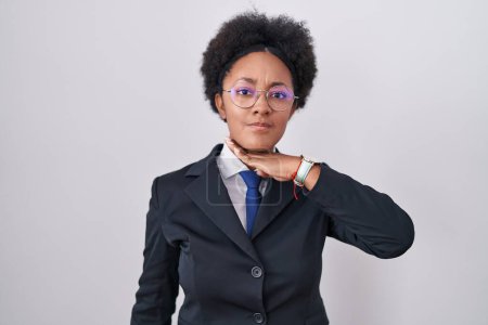 Téléchargez les photos : Belle femme africaine aux cheveux bouclés portant une veste d'affaires et des lunettes tranchant la gorge avec la main comme un couteau, menace d'agression avec une violence furieuse - en image libre de droit