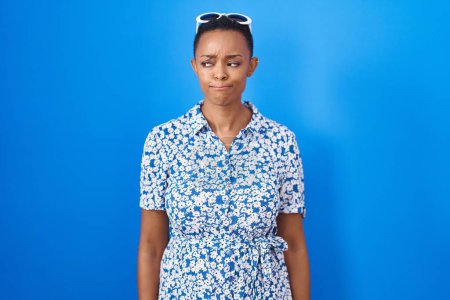 Foto de African american woman standing over blue background smiling looking to the side and staring away thinking. - Imagen libre de derechos
