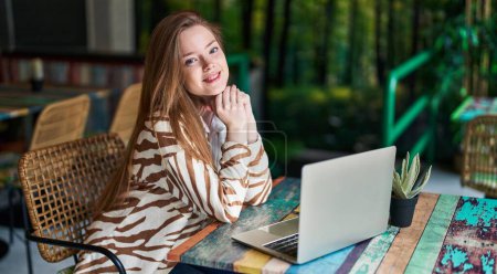 Téléchargez les photos : Jeune femme caucasienne utilisant ordinateur portable assis sur la table au restaurant - en image libre de droit