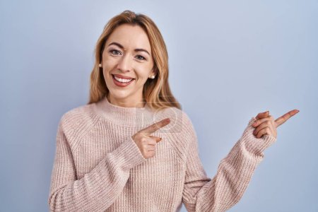 Photo for Hispanic woman standing over blue background smiling and looking at the camera pointing with two hands and fingers to the side. - Royalty Free Image