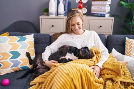 Téléchargez les photos : Young blonde woman hugging dog sitting on sofa at home - en image libre de droit