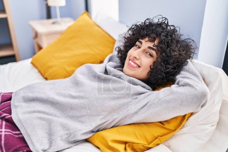Téléchargez les photos : Jeune femme du Moyen-Orient détendue avec les mains sur la tête couchée sur le lit dans la chambre - en image libre de droit