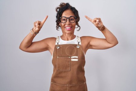 Photo for Middle age woman wearing apron over white background smiling amazed and surprised and pointing up with fingers and raised arms. - Royalty Free Image