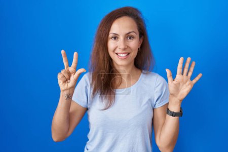 Photo for Brunette woman standing over blue background showing and pointing up with fingers number eight while smiling confident and happy. - Royalty Free Image
