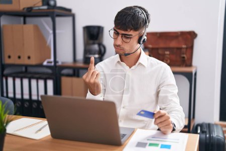 Photo for Young hispanic man working using computer laptop holding credit card showing middle finger, impolite and rude fuck off expression - Royalty Free Image