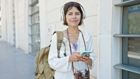 Téléchargez les photos : Jeune belle hispanique femme touriste souriant confiant écouter de la musique à la rue - en image libre de droit