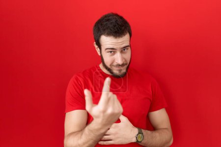 Foto de Joven hombre hispano con camiseta roja casual haciendo señas ven aquí gesto con la mano invitando a la bienvenida feliz y sonriente - Imagen libre de derechos