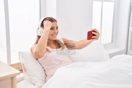 Photo for Young beautiful hispanic woman playing video game sitting on bed at bedroom - Royalty Free Image