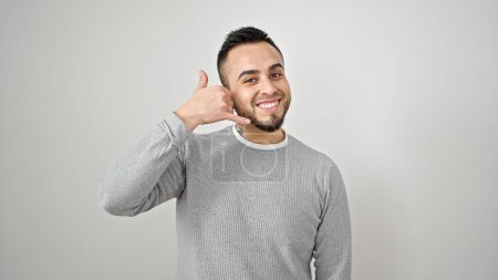 Foto de Hombre hispano sonriendo confiado haciendo gesto telefónico con la mano sobre fondo blanco aislado - Imagen libre de derechos