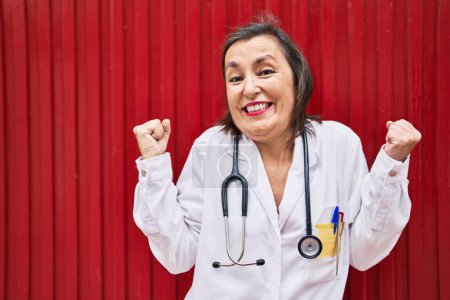 Photo for Middle age hispanic woman wearing doctor uniform and stethoscope screaming proud, celebrating victory and success very excited with raised arm - Royalty Free Image
