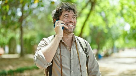 Téléchargez les photos : Jeune homme hispanique touriste portant un sac à dos parlant sur smartphone au parc - en image libre de droit