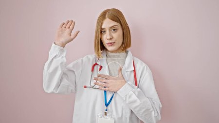 Foto de Joven doctora rubia haciendo un juramento con la mano en el pecho sobre un fondo rosa aislado - Imagen libre de derechos