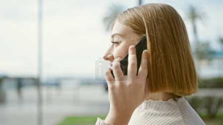 Téléchargez les photos : Jeune femme blonde parlant sur smartphone à la rue - en image libre de droit