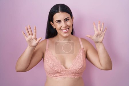 Photo for Young hispanic woman wearing pink bra showing and pointing up with fingers number ten while smiling confident and happy. - Royalty Free Image