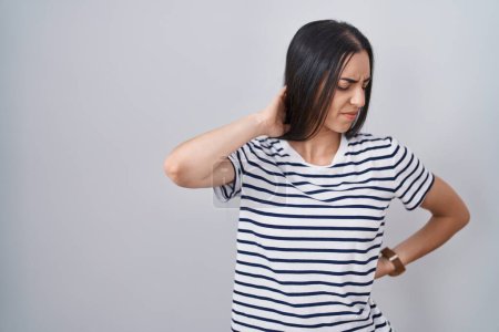 Photo for Young brunette woman wearing striped t shirt suffering of neck ache injury, touching neck with hand, muscular pain - Royalty Free Image