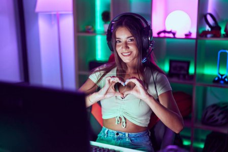 Photo for Young beautiful hispanic woman streamer smiling confident doing heart symbol with hands at gaming room - Royalty Free Image