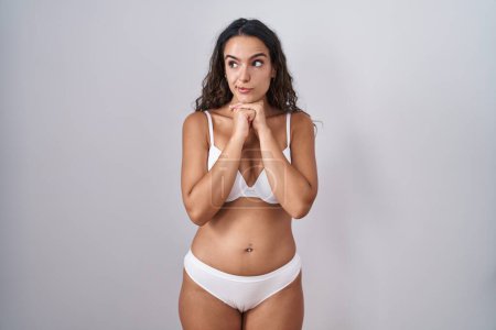 Photo for Young hispanic woman wearing white lingerie laughing nervous and excited with hands on chin looking to the side - Royalty Free Image