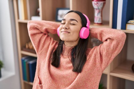 Téléchargez les photos : Jeune femme hispanique écoutant de la musique assise sur la table à la maison - en image libre de droit